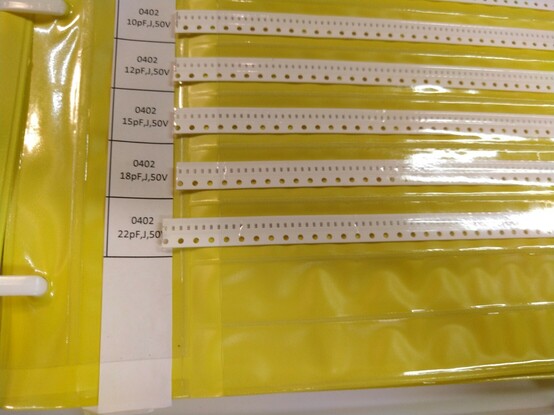 A slightly extended tape of 0402 sized ceramic capacitors extending from it's pocket on an SMD sample book, showing that one of them has been used.