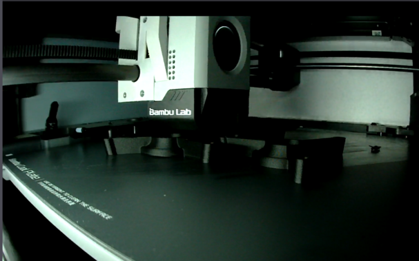 Inside of a Bambu Lan 3D printer. Three mysterious shapes are being created out of black carbon-fibre-filled PLA